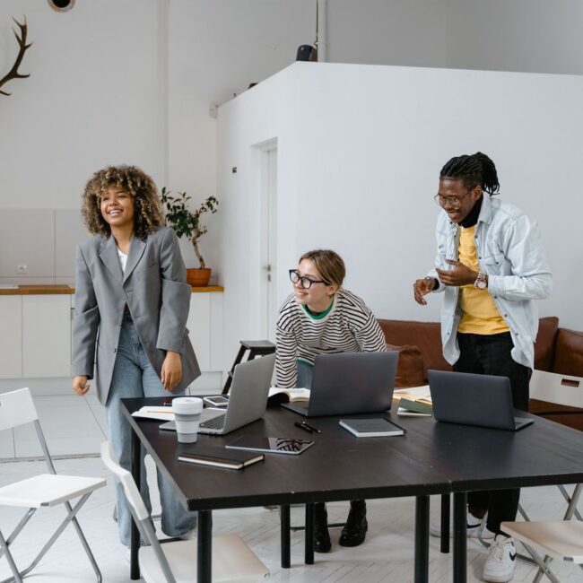 Trois personnes échangent dans un espace de travail lumineux, ordinateurs portables sur la table
